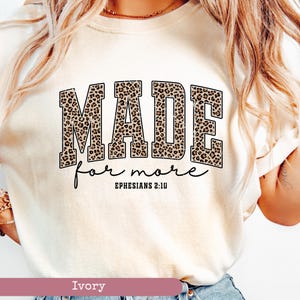 K&ouml;nnte beinhalten: Elfenbeinfarbenes T-Shirt mit dem Schriftzug "MADE for more" in einem Leopardenmuster. Der Text "Ephesians 2:10" steht darunter in einer handschriftlichen Schriftart. Das T-Shirt hat einen Rundhalsausschnitt.