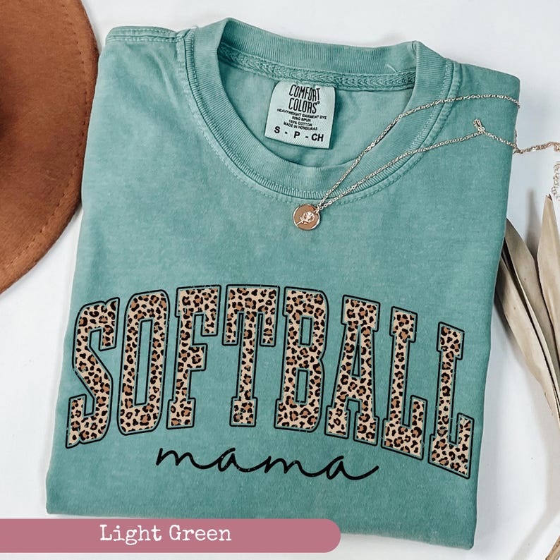 May include: Light green t-shirt with the words "Softball mama" in black letters with a leopard print design.