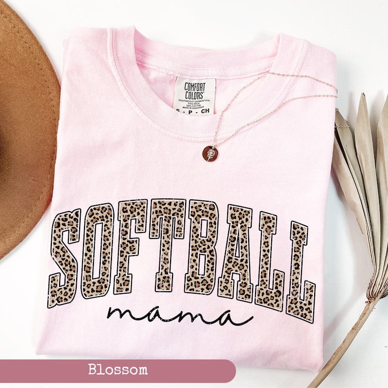 May include: Pink t-shirt with the words "Softball mama" in black text with a leopard print design. The words "Softball" are in a large, bold font.
