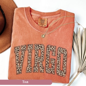 Może przedstawiać: Pomarańczowy t-shirt z nadrukiem słowa "VIRGO" dużymi, pogrubionymi literami. Litery są wypełnione wzorem w panterkę. Koszulka jest marki Comfort Colors.