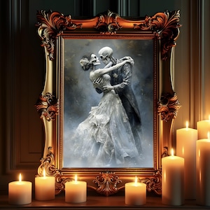 May include: A framed artwork depicts a skeletal couple embracing in a romantic pose. The ornate gold frame surrounds the image, and several lit candles are placed in front of the artwork, creating a warm glow.