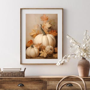 May include: A framed print featuring a still life of white pumpkins and autumn leaves. The pumpkins vary in size, with a large one in the center and smaller ones around it. The leaves are in shades of orange and yellow.