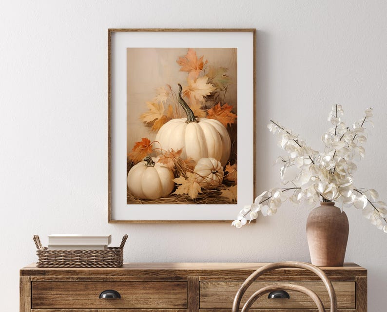 May include: A framed print featuring a still life of white pumpkins and autumn leaves. The pumpkins vary in size, with a large one in the center and smaller ones around it. The leaves are in shades of orange and yellow.