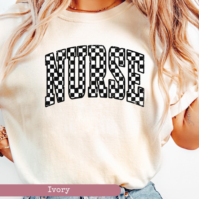 May include: A white t-shirt with the word "NURSE" printed in black and white chequered pattern. The shirt is a light ivory colour.