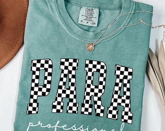 May include: Light green t-shirt with the word "PARA" in large, black and white checkered letters, and the word "professional" in cursive below. A silver necklace with a pendant is on the shirt.