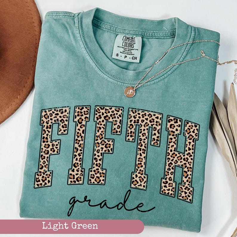 May include: Light green t-shirt with a leopard print "FIFTH grade" graphic.