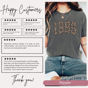 Op de afbeelding: Een grijs T-shirt met een luipaardprint met het jaar "1995". Het shirt wordt gedragen door een model in blauwe jeans. Klantbeoordelingen worden weergegeven met positieve feedback over de kwaliteit, pasvorm en het comfort van het shirt.