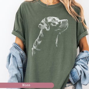 May include: A green t-shirt with a white outline drawing of a Labrador Retriever dog looking up. The dog's head and neck are visible. The shirt has a relaxed fit and short sleeves.