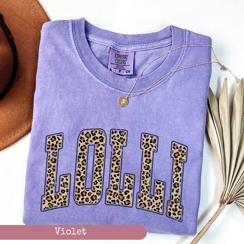 May include: A purple t-shirt with the word "LOLLI" printed in a leopard print design. The shirt is made by Comfort Colors.