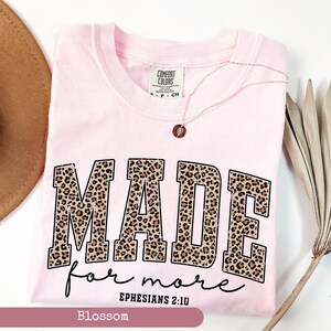 K&ouml;nnte beinhalten: Ein hellrosa T-Shirt mit den Worten "MADE for more" in einem Leopardenmuster. Der Text "Epheser 2:10" steht unter dem Haupttext. Das Shirt ist von der Marke Comfort Colors.