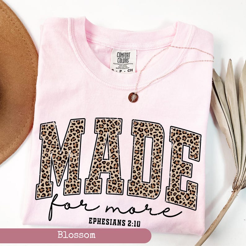 K&ouml;nnte beinhalten: Ein hellrosa T-Shirt mit den Worten "MADE for more" in einem Leopardenmuster. Der Text "Epheser 2:10" steht unter dem Haupttext. Das Shirt ist von der Marke Comfort Colors.