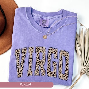 Może przedstawiać: Fioletowy T-shirt z nadrukiem słowa "VIRGO" w wzorze panterki. Koszulka jest marki Comfort Colors i jest w rozmiarze S.