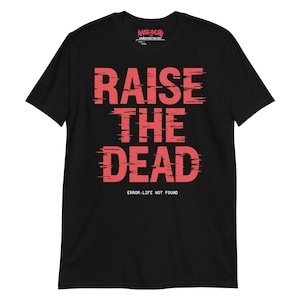 May include: Black t-shirt featuring the words "RAISE THE DEAD" in a distressed red font. The phrase "ERROR: LIFE NOT FOUND" is printed below. The shirt has a crew neck and short sleeves.
