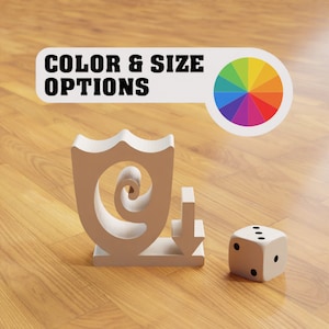 Puede incluir: Escudo de madera blanco con un diseño en espiral y una flecha hacia abajo. El escudo está sobre una superficie de madera con una rueda de colores y un dado blanco con puntos negros.