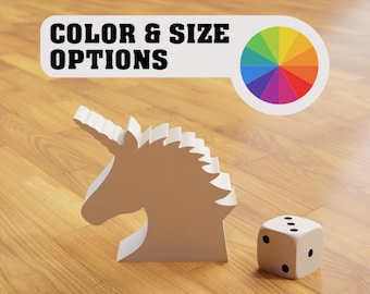 May include: A white unicorn-shaped object and a white die with black dots sit on a wooden surface. The image includes a banner that reads "COLOR & SIZE OPTIONS" with a color wheel.