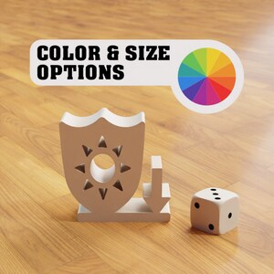 Puede incluir: Un escudo blanco con un dise&ntilde;o de sol y una flecha blanca apuntando hacia abajo. El escudo y la flecha est&aacute;n sobre una superficie de madera. Un dado blanco con puntos negros est&aacute; a la derecha del escudo y la flecha. El texto "COLOR & SIZE OPTIONS" est&aacute; encima del escudo y la flecha. Una rueda de colores est&aacute; a la derecha del texto.