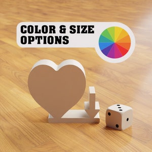 Peut inclure: Un objet en forme de c&oelig;ur blanc avec une fl&egrave;che blanche pointant vers le bas, et un d&eacute; blanc avec des points noirs sur une surface en bois. Le texte "COLOR & SIZE OPTIONS" est visible au-dessus du c&oelig;ur et de la fl&egrave;che. Une roue chromatique color&eacute;e est visible &agrave; droite du texte.