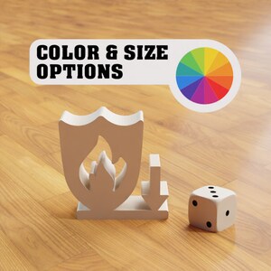 May include: A white shield with a flame inside, a white arrow pointing down, and a white dice with black dots on a wooden surface. The text "COLOR & SIZE OPTIONS" is visible above the shield.