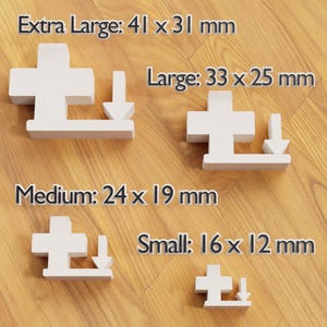 May include: Four white, cross-shaped wooden puzzle pieces of varying sizes, each with a downward-pointing arrow. Sizes are labeled: Extra Large (4.1 x 3.1 cm), Large (3.3 x 2.5 cm), Medium (2.4 x 1.9 cm), and Small (1.6 x 1.2 cm).