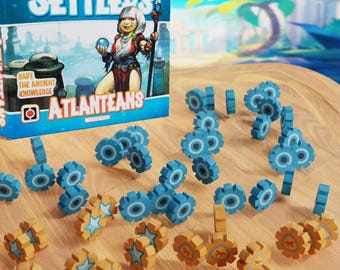May include: A game box for Imperial Settlers: Atlanteans, featuring a woman with a spear and a blue background. The box is open and shows blue and gold game pieces, including gears and stars.