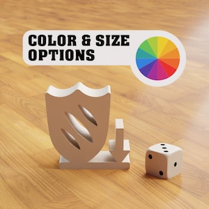 May include: A white shield with three lines carved into it, a white arrow pointing down, and a white die with black dots on a wood surface. The text "COLOR & SIZE OPTIONS" is above the shield and a rainbow color wheel is to the right of the shield.