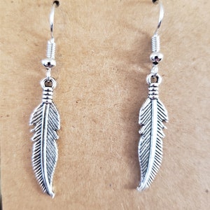 May include: A pair of silver feather earrings with a simple hook design.