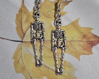 Puede incluir: Un par de pendientes de esqueleto de plata. Los pendientes son de estilo colgante y presentan un diseño de esqueleto detallado.