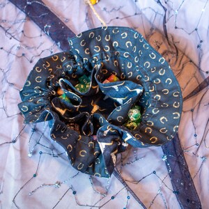 May include: A black and gold fabric dice bag with a horseshoe pattern. The bag is open and filled with colorful dice.