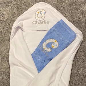 May include: A white hooded towel with a blue towel inside. Both towels have the letter "C" embroidered on them with stars and the name "Charlie" embroidered on the hooded towel.