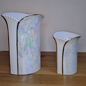 May include: Two white ceramic vases with a pearlescent iridescent glaze and gold trim. The larger vase is taller and wider than the smaller vase.