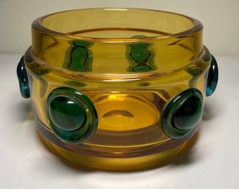 May include: A round amber glass bowl with a textured surface and green glass circles around the rim.