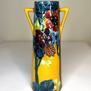Könnte beinhalten: Eine gelbe Keramikvase mit zwei Henkeln und einem Blumendesign. Die Vase ist mit blauen, grünen, roten und braunen Blumen und Blättern verziert. Die Vase ist unten mit dem Wort "Royal" gekennzeichnet.