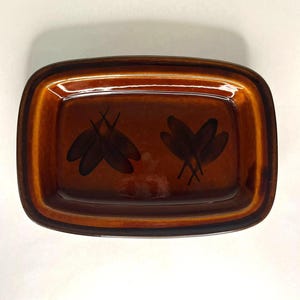 May include: A rectangular brown ceramic dish with a glossy finish. It has a darker brown rim and two black leaf designs. The interior is a lighter shade of brown. A decorative piece.
