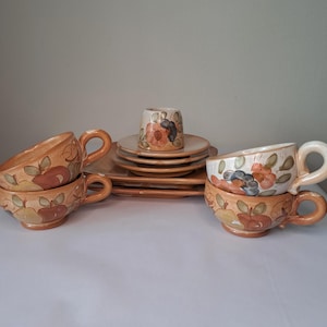 May include: A ceramic tea set with cups, saucers, and plates. The set has a hand-painted floral design in orange, red, and green. It includes two teacups with handles, and a small cup. The plates and saucers are square.