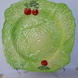 May include: A green ceramic salad plate shaped like a head of lettuce with three red tomatoes. The plate is perfect for serving salads or other dishes.