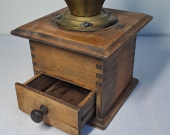Op de afbeelding: Antiek houten koffiemolen met een messing bovenkant en een lade om gemalen koffie op te bergen.