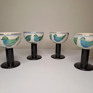 May include: Four ceramic goblets. Each has a white bowl, black stem, and base. The bowls are decorated with a blue bird design and green accents. The rim is trimmed with gold.