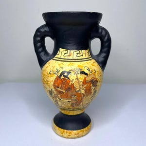 May include: A black and yellow ceramic vase with two handles. The vase features a painted scene of figures in red and orange robes. The rim and base are black, and the body is yellow with a decorative border.