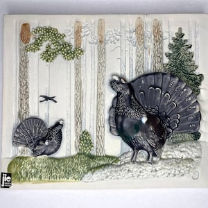 以下が含まれることがあります： 雪が降った森の中に、2羽のライチョウが描かれた白いセラミックタイル。ライチョウは、羽根のディテールやリアルな特徴が表現されています。タイルは、表面がテクスチャ加工されており、縁が盛り上がっています。