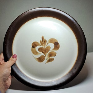 May include: A white ceramic dinner plate with a brown rim and a brown floral design in the center.