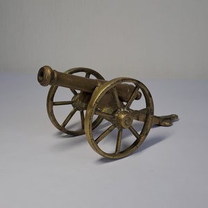 May include: A small, brass cannon with wheels. The cannon is detailed with a barrel, wheels, and a carriage.