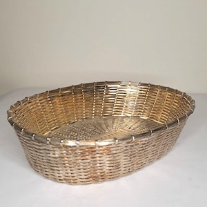 Può includere: Un cestino ovale intrecciato con finitura metallica oro e argento. Il cestino presenta un motivo a trama fitta e una struttura robusta. Misura circa 30 cm di lunghezza e 20 cm di larghezza, adatto a vari usi.