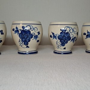 Puede incluir: Juego de cuatro tazas de cerámica blanca con diseños de uvas azules. Las tazas tienen una forma redondeada y un borde azul.