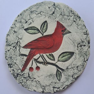 May include: A ceramic wall plaque featuring a red cardinal perched on a branch with green leaves and red berries. The background is a white and black cracked glaze.