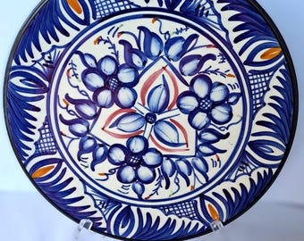 May include: A white ceramic plate with a blue and white floral design. The plate has a black rim and is decorated with a repeating pattern of flowers and leaves.