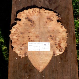 May include: Two pieces of raw, unfinished wood with a natural edge, joined to form a heart shape. The wood has a light brown color with darker knots and grain patterns. A handwritten note indicates the dimensions: 11 inches long, 9.5 inches wide, and approximately 4 mm thick.