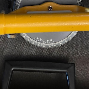May include: A yellow level with a black handle and a circular protractor with markings in degrees. The protractor is labeled "R" and "L" and has markings from 0 to 90 degrees.