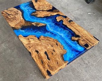 May include: A rectangular wooden table top with a blue epoxy resin river flowing through the center. The wood has a natural grain pattern and the resin has a glossy finish.