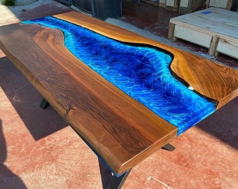Puede incluir: Una mesa de madera grande con un río de epoxi azul que recorre el centro. La mesa tiene patas de metal negro.