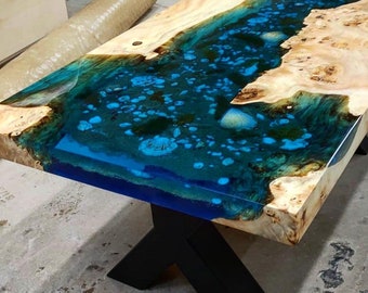 May include: A wooden coffee table with a blue and green epoxy resin river design. The table has a black X-shaped base.